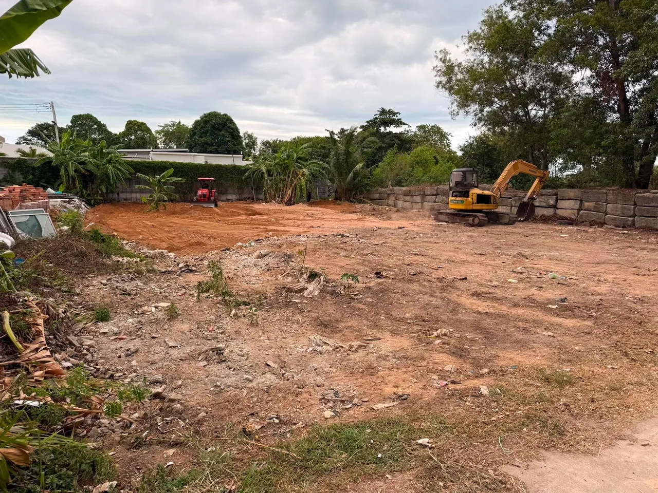 Tractor spreading the delivered soil while the excavator works along the retaining wall