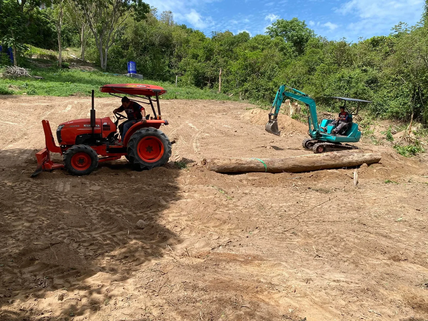 Kubota tractor pulling a large felled log across the cleared area